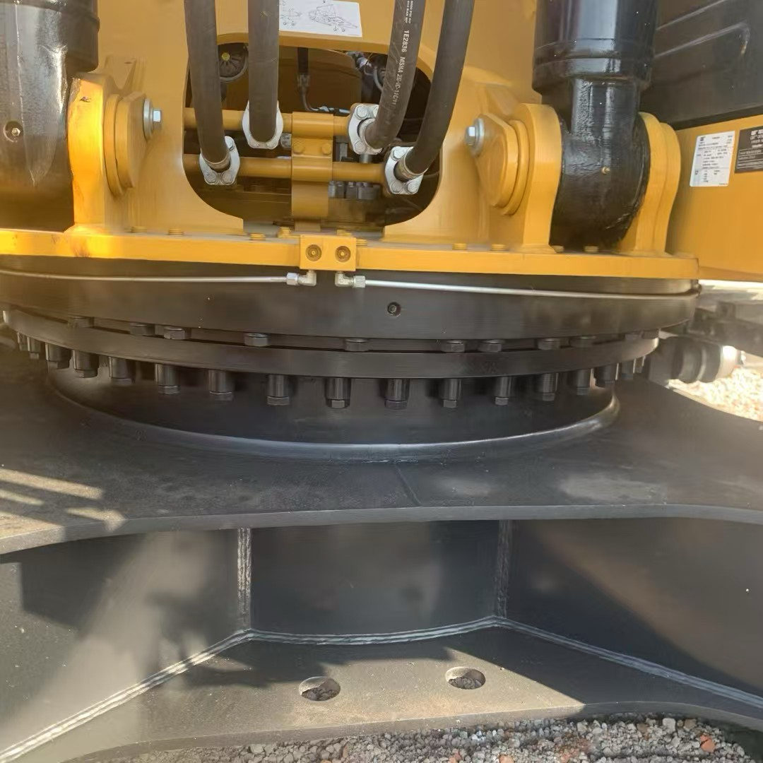 Close-up of Caterpillar excavator swing bearing, slewing ring, hydraulic hoses, and mounting bolts