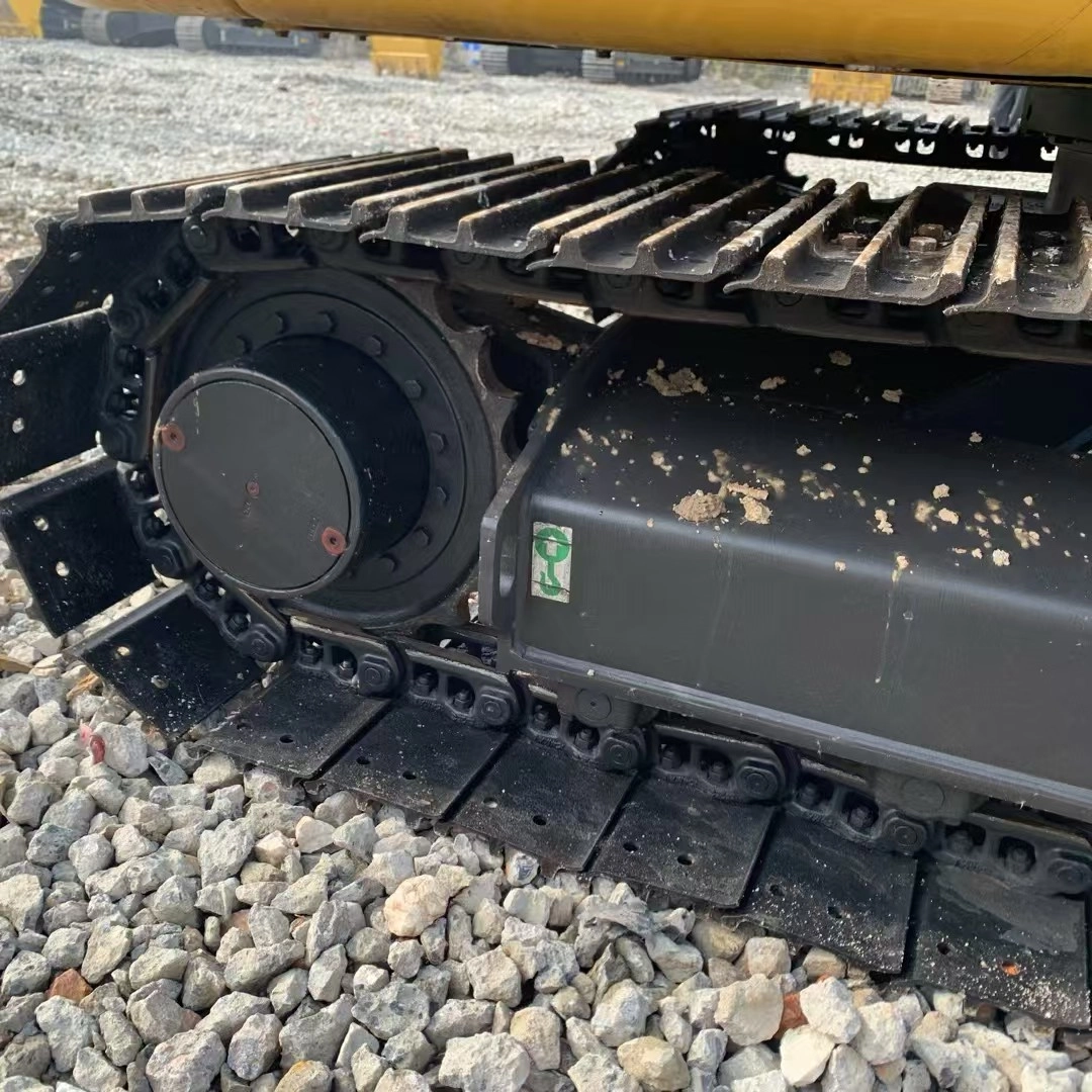 Excavator undercarriage showing steel tracks, sprocket, and final drive motor on gravel surface.