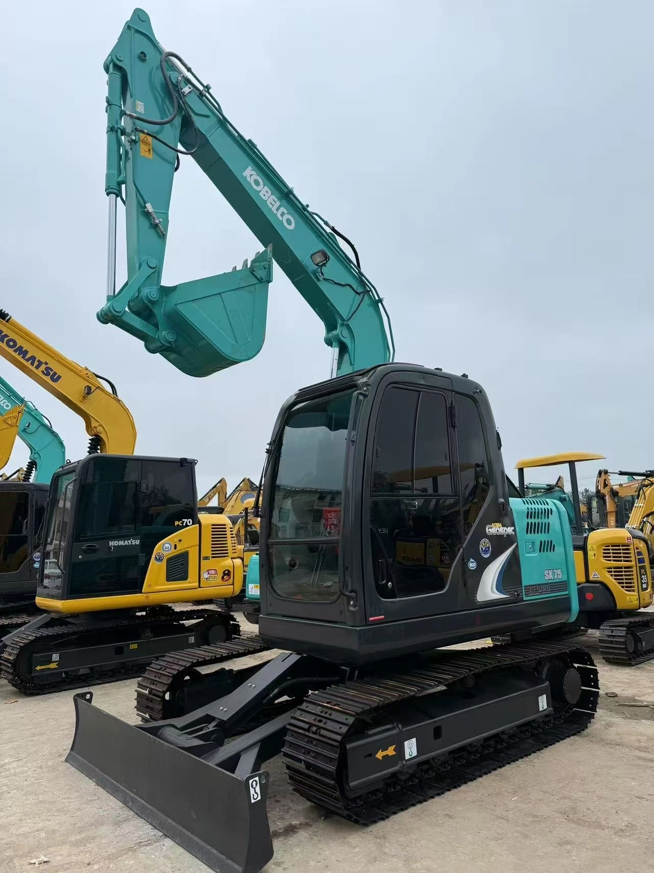Kobelco SK75 excavator full body parked in outdoor machinery yard, excellent condition.